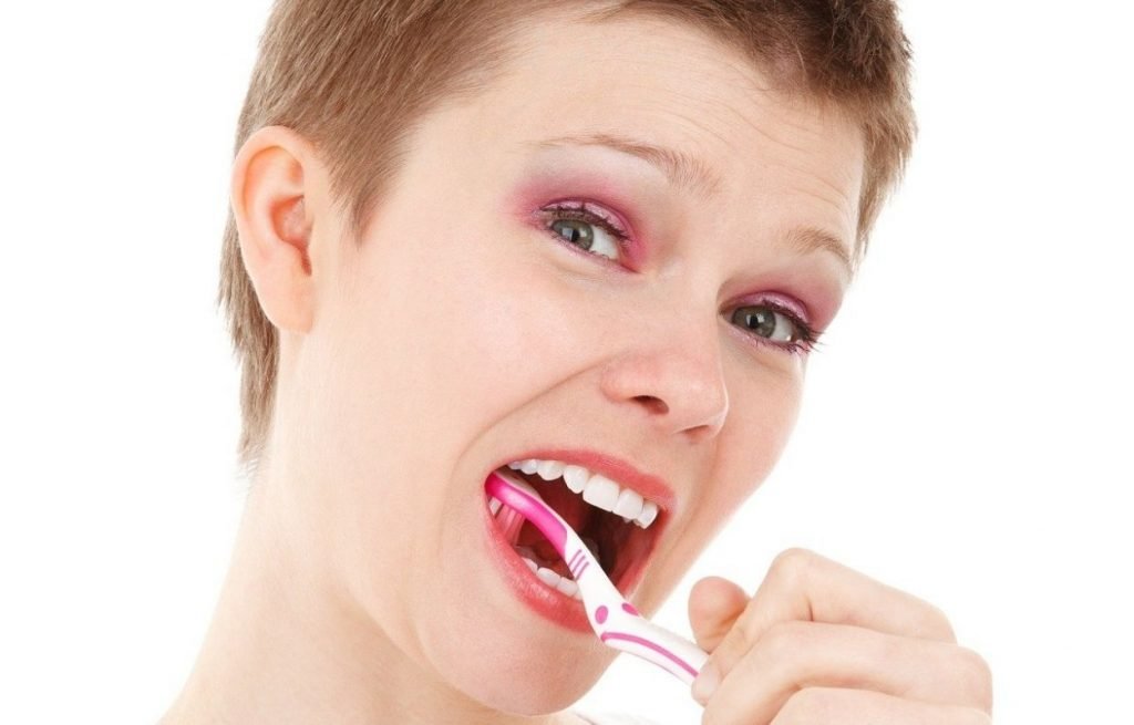 Imagem mostra mulher escovando os dentes - sonhar com dente quebrado
