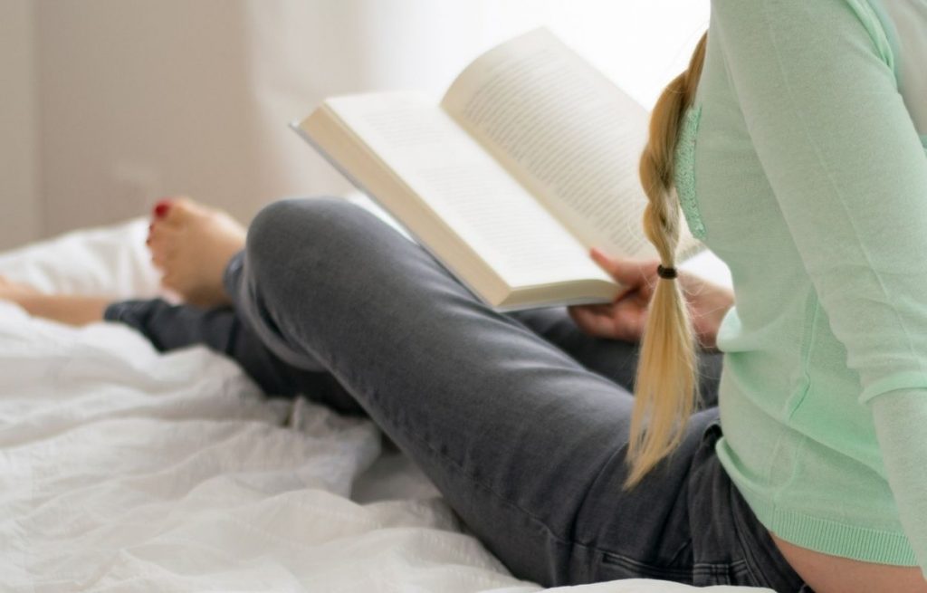 Imagem mostra mulher lendo na cama - afirmações antes de dormir