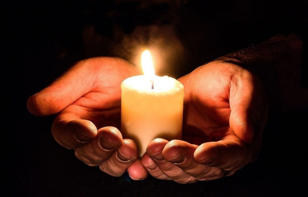 Imagem mostra mãos em prece com vela - oração para afastar o mal