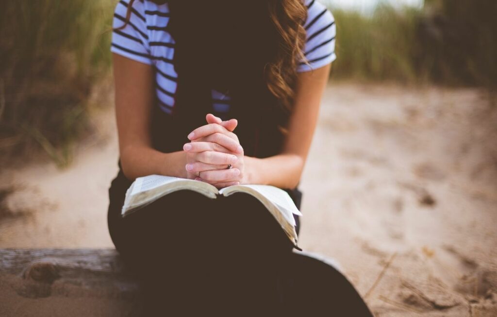 Imagem mostra mulher com bíblia e mãos em prece - salmos para acalmar