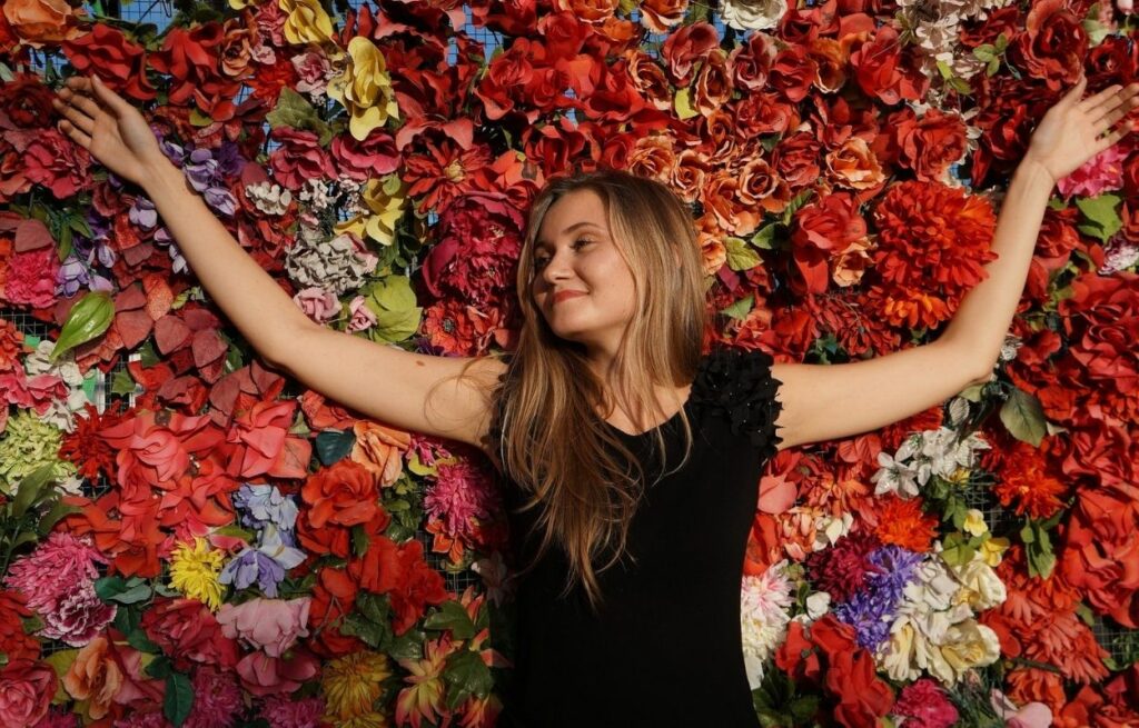 Imagem mostra mulher em meio a flores - frases para foto com flor
